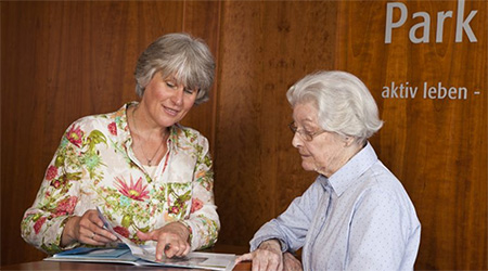 Das Bild zeigt eine Mitarbeiterin der Senioren-Wohnanlage Haus am Park in Haan, wie sie einer Mieterin die Extras erklärt.