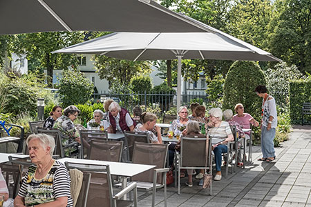 Ein Gruppe älterer Menschen sitzen gemeinsam am Kaffeetisch im Garten der Seniorenwohnanlage Haus am Park in Haan